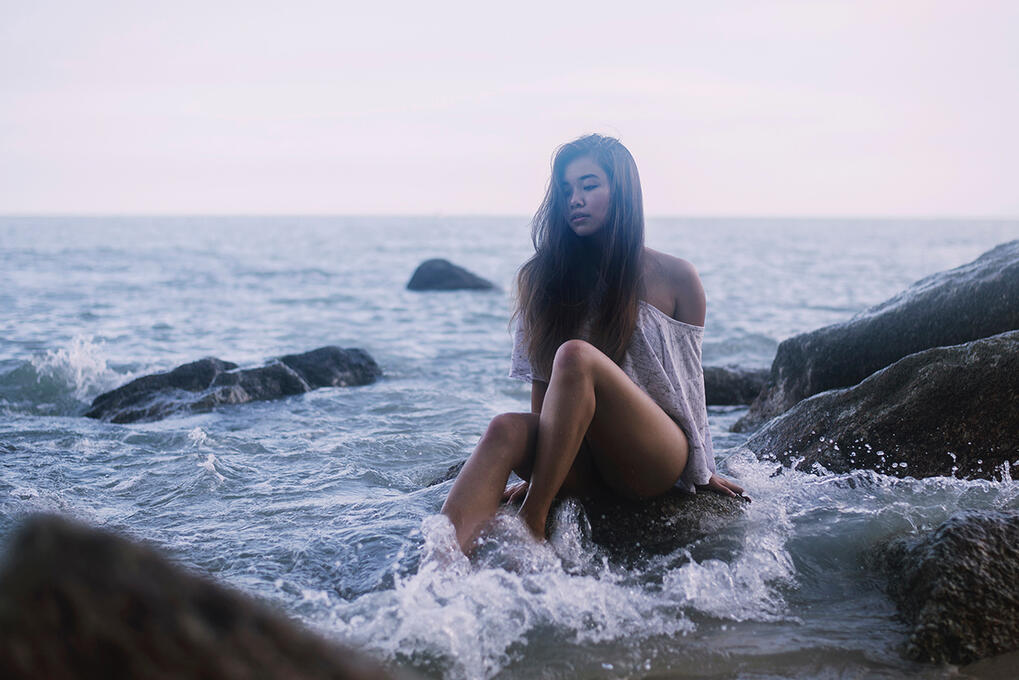 long-haired girl sitting on a rock with small waves crashing around, , by tayylin.com